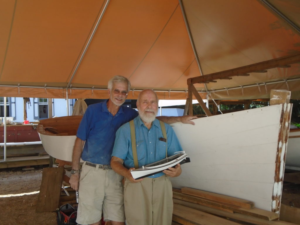 Model builder Ralph Koebke (right) and his hull model of the Florida skipjack in front of the full size replica currently under contruction at the lighthouse Heritage Boatworks program. Volunteer boat builder Richard Sexauer (left) can be seen working on the full size replica most morning at the lighthouse.